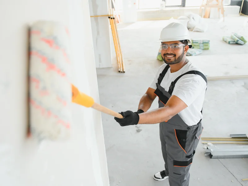Professional painter applying yellow paint to drywall in commercial construction project