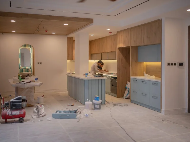 A modern kitchen undergoing renovation, featuring a worker, tools, and materials