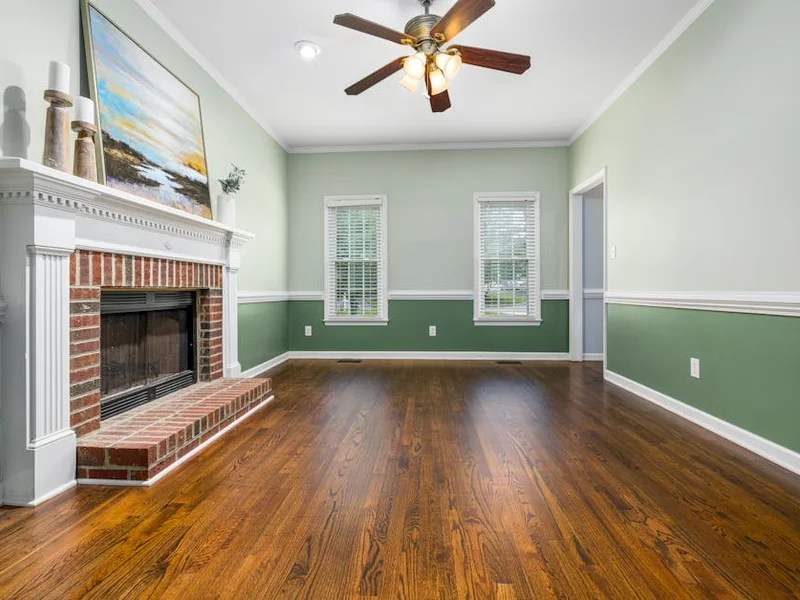 A cozy empty living room featuring a brick fireplace, wooden floors, and elegant decor.
