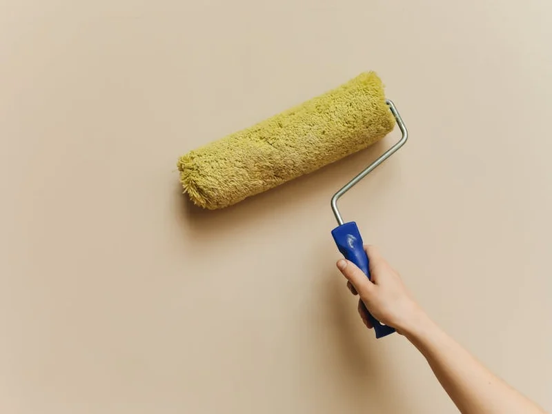 A hand using a yellow paint roller to apply white paint on a wall. Perfect for DIY and home improvement themes.
