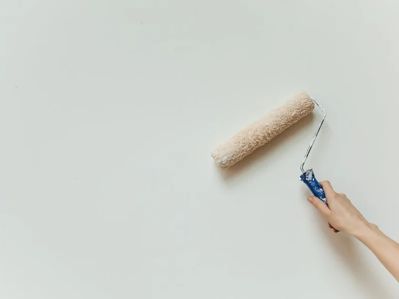 Close-up of a hand painting a wall with a roller brush during renovation.