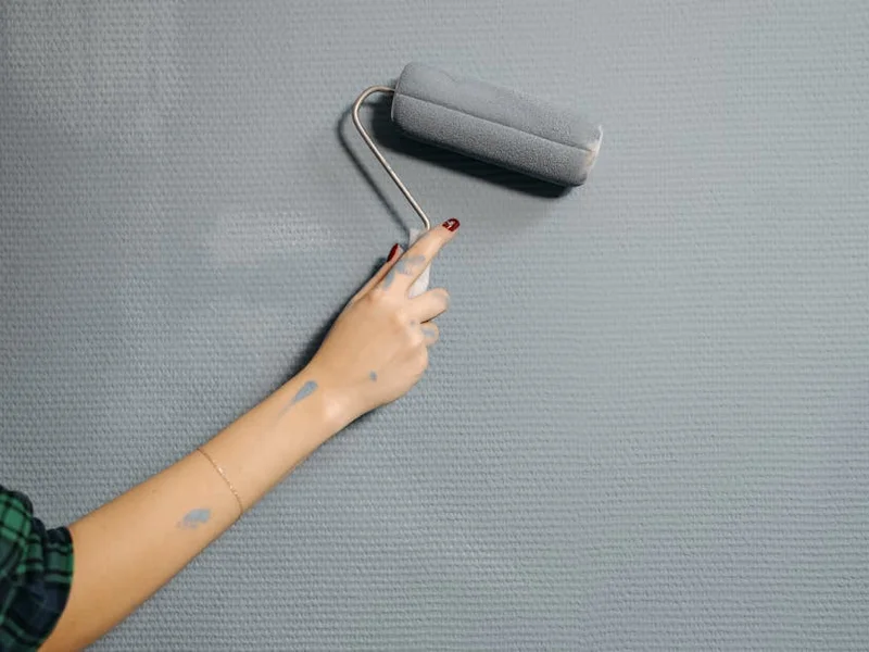 A close-up of a person's hand using a paint roller on a blue wall for home renovation.