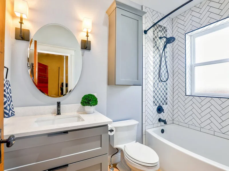 Elegant modern bathroom featuring chevron tiles, oval mirror, and sleek fixtures for a contemporary look