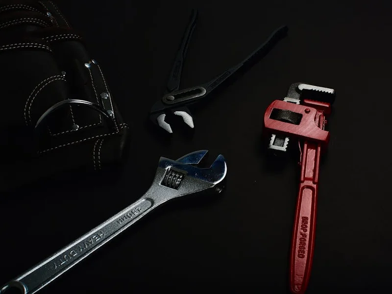 Close-up of various hand tools including wrenches and pliers on a dark surface