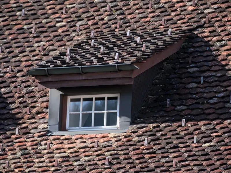 Close-up of a vintage rooftop with a dormer window, showcasing unique tile arrangement and architectural details.
