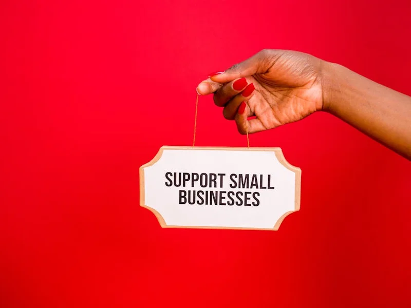 A hand holds a sign that reads 'Support Small Businesses' against a vibrant red background.