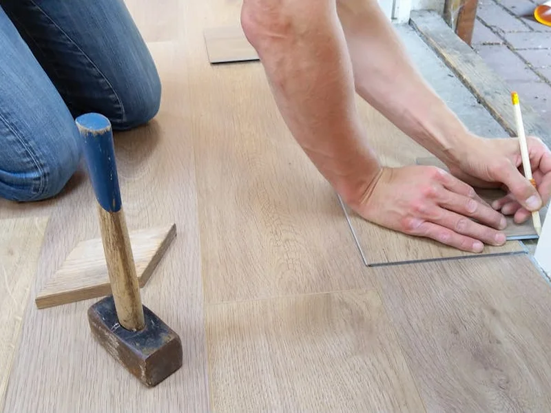 A craftsman carefully measures and marks wooden floor panels for precise installation.