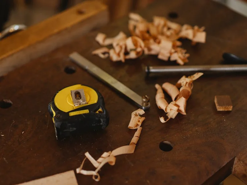 From above of tape measure near metal carpentry instruments with wooden shavings in workshop